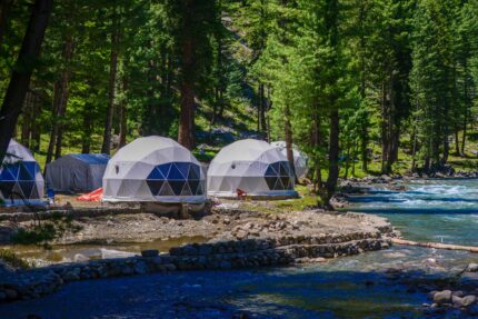 campement de dômes géodésiques dans une forêt au bord d'une rivière